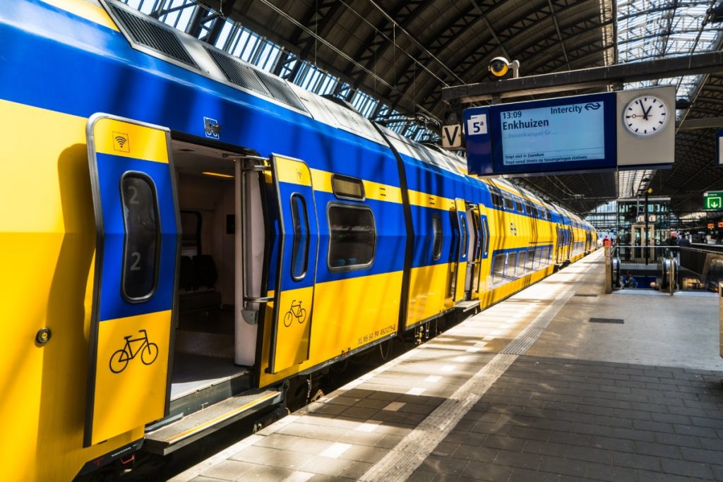 Gult nederlandsk tog på Amsterdam Centraal stasjon om morgenen.