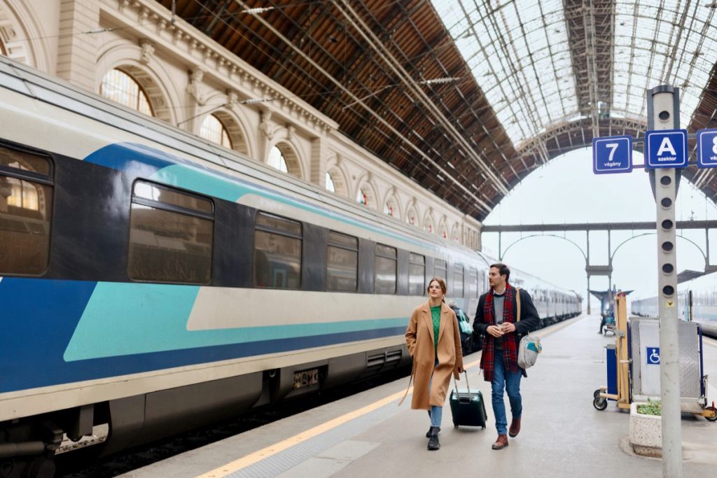 Venner går smilende langs togperrongen på ungarsk jernbanestasjon.