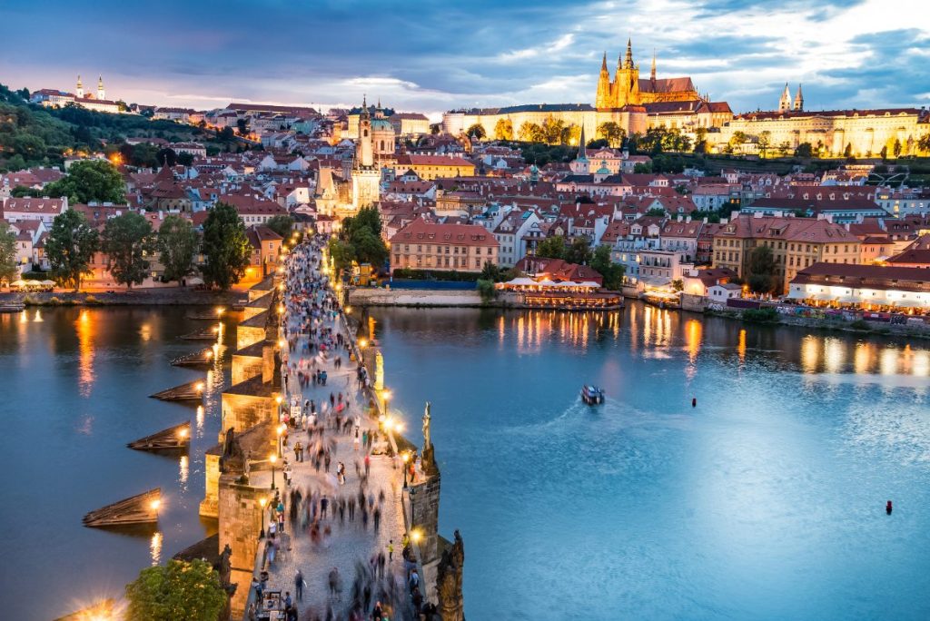 Praha med røde takstein og spirende tårn i kveldslys.